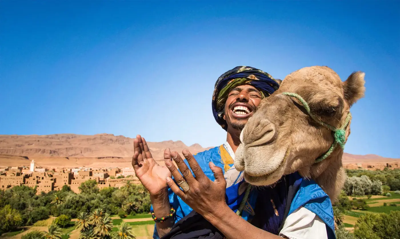 Smiling local guide laughing with a camel in front of a Moroccan kasbah